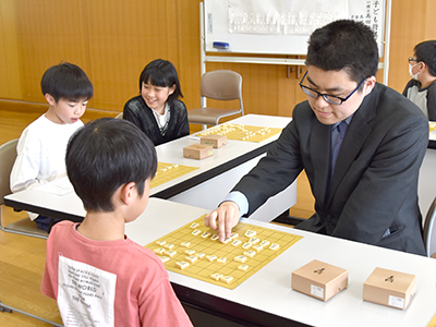 指導対局を行う棋士と児童の写真