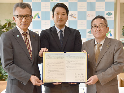 協定書を手に持ち記念撮影を受ける3人