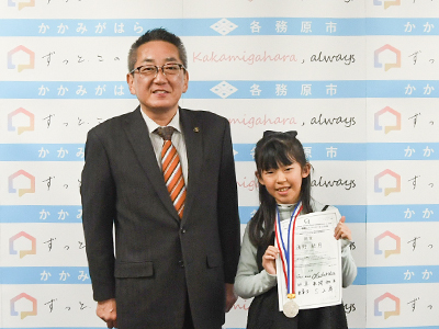 受賞メダルと賞状を掲げる淺野さんと、浅野市長